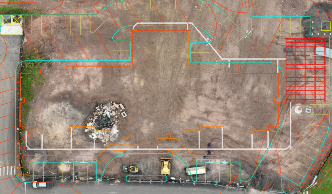 Orthomosaic of a cleared building pad with the civil design registered on top: building footprint, utility runs, curb lines, and parking layout