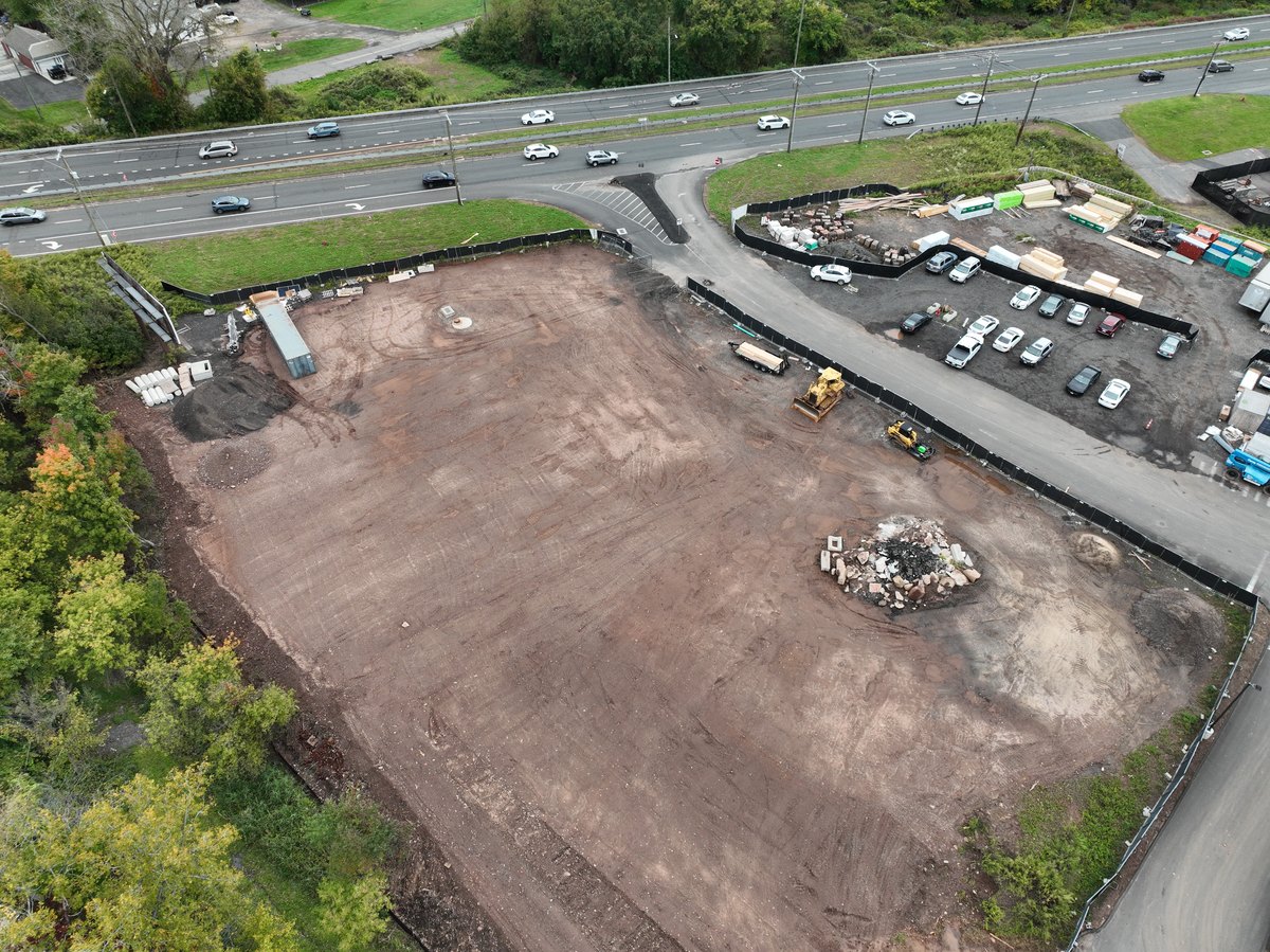 Aerial oblique of a cleared and graded development site with its highway frontage, access drive, and perimeter controls in frame