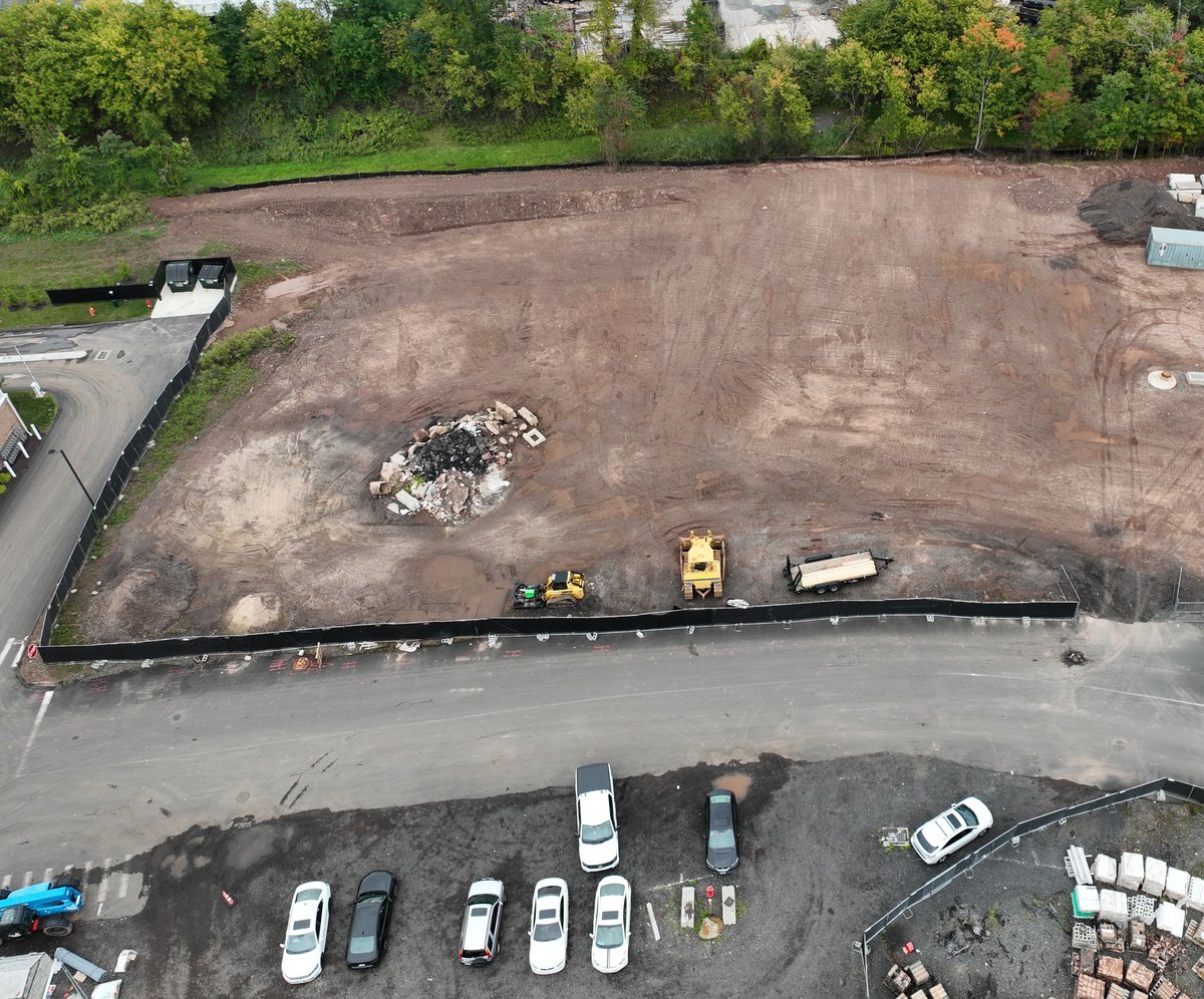 Near-vertical aerial of a cleared and graded site showing the finished grade, perimeter silt fence, earthmoving equipment, and material staging