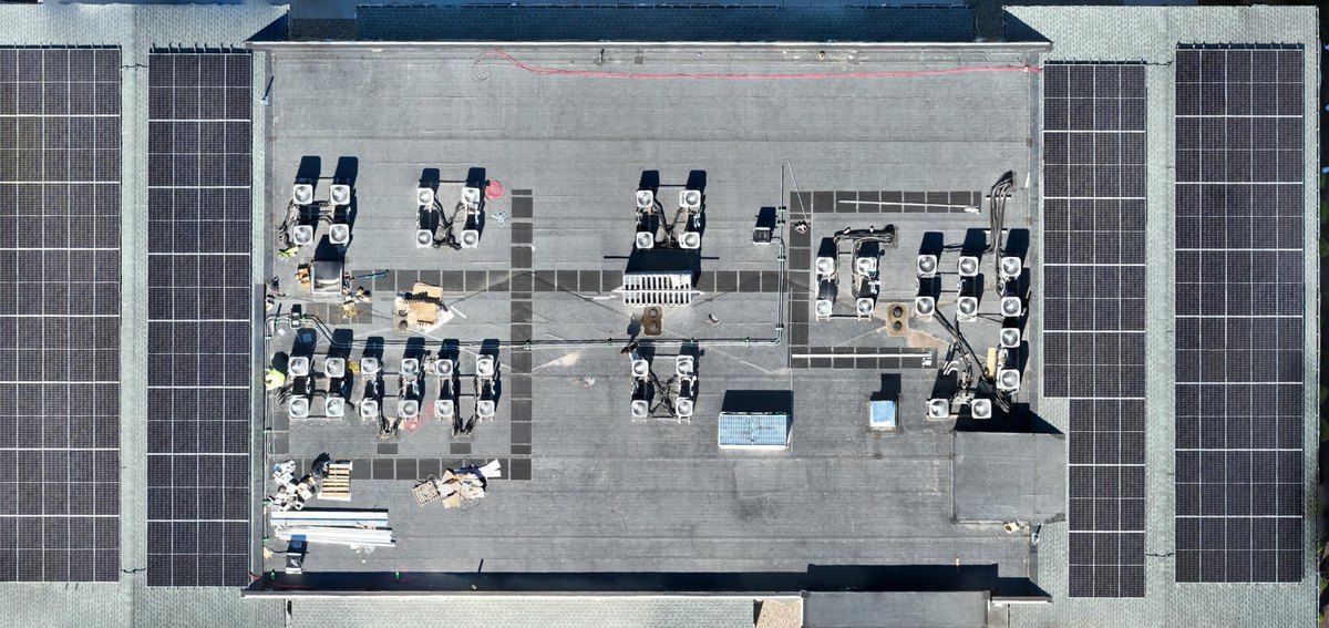 Levelled orthomosaic of a full commercial roof from directly overhead, parapet to parapet, with solar arrays along both flanks, a central mechanical zone of rooftop units, walkway pads, and drains