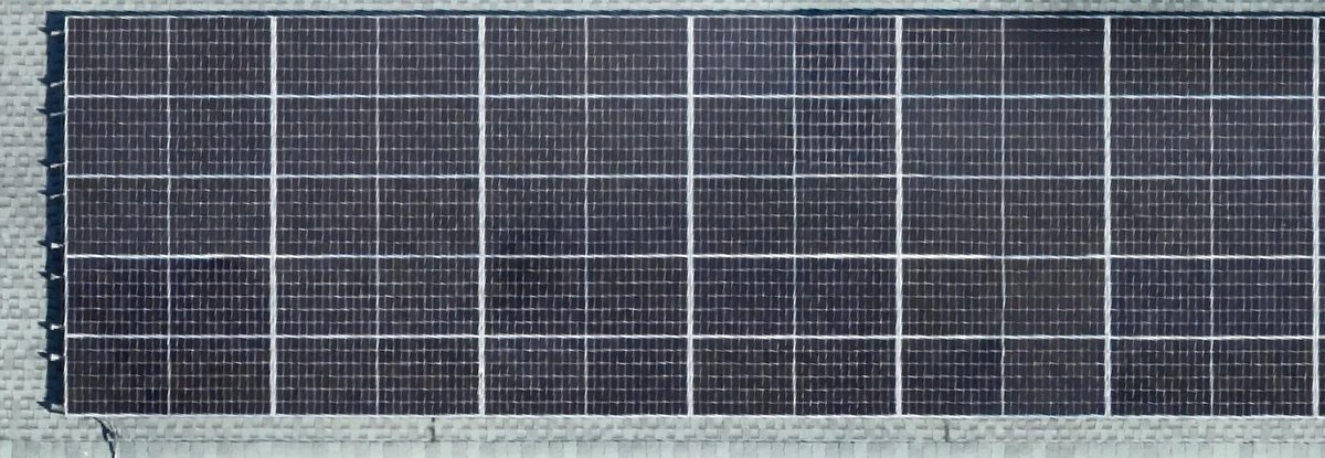 Orthomosaic detail of a rooftop solar array run, individual modules and cells resolved, with mounting rails, end clamps, and the roof surface either side of the array