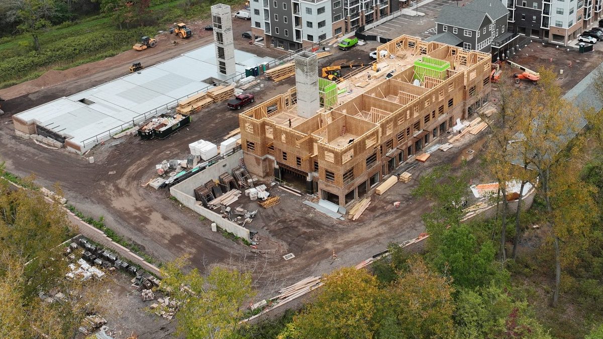 Close aerial of an active wood framing area showing open floor edges, material laydown, and equipment