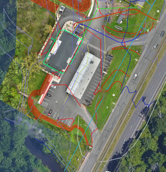 Orthomosaic of existing commercial buildings with the civil layer registered on top: contours, utilities, drainage, and the watercourse along the rear of the property